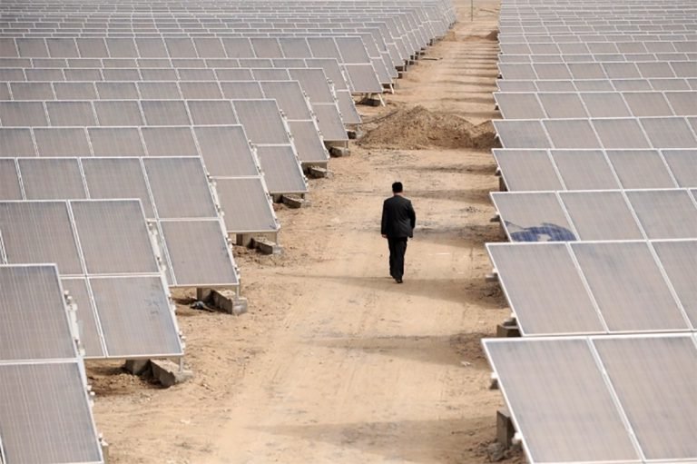 A man walks among solar panels at a solar power plant under construction in Aksu, Xinjiang in the Uighur Autonomous Region